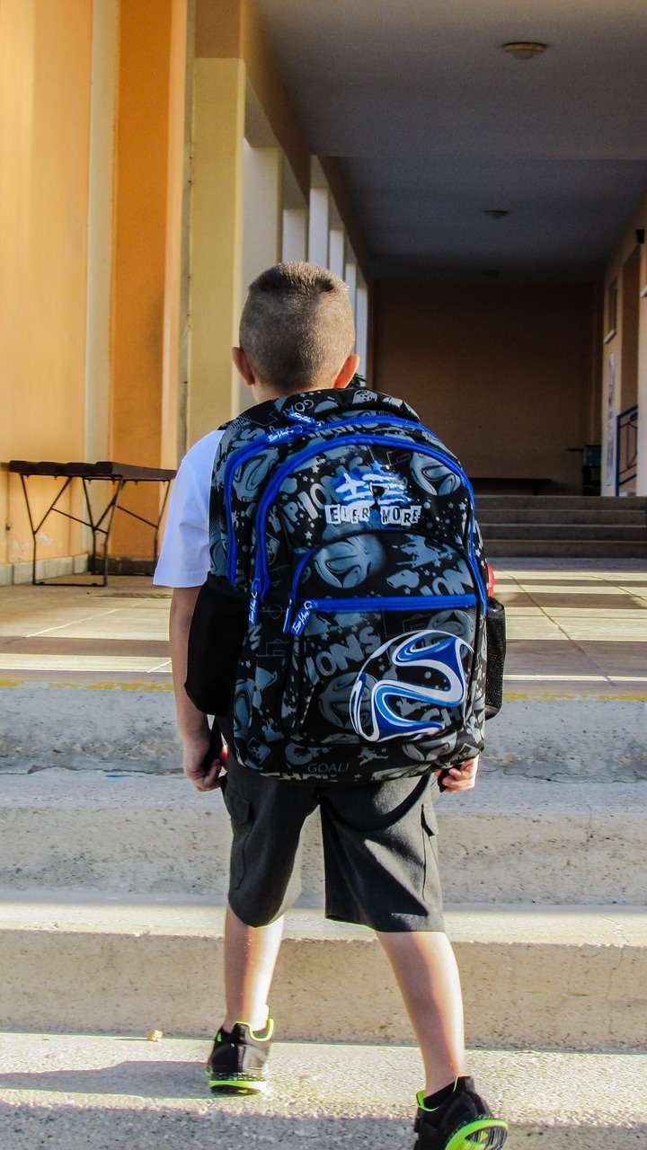 Schulkind von hinten fotografiert mit Schulranzen auf dem Rücken betritt Schule